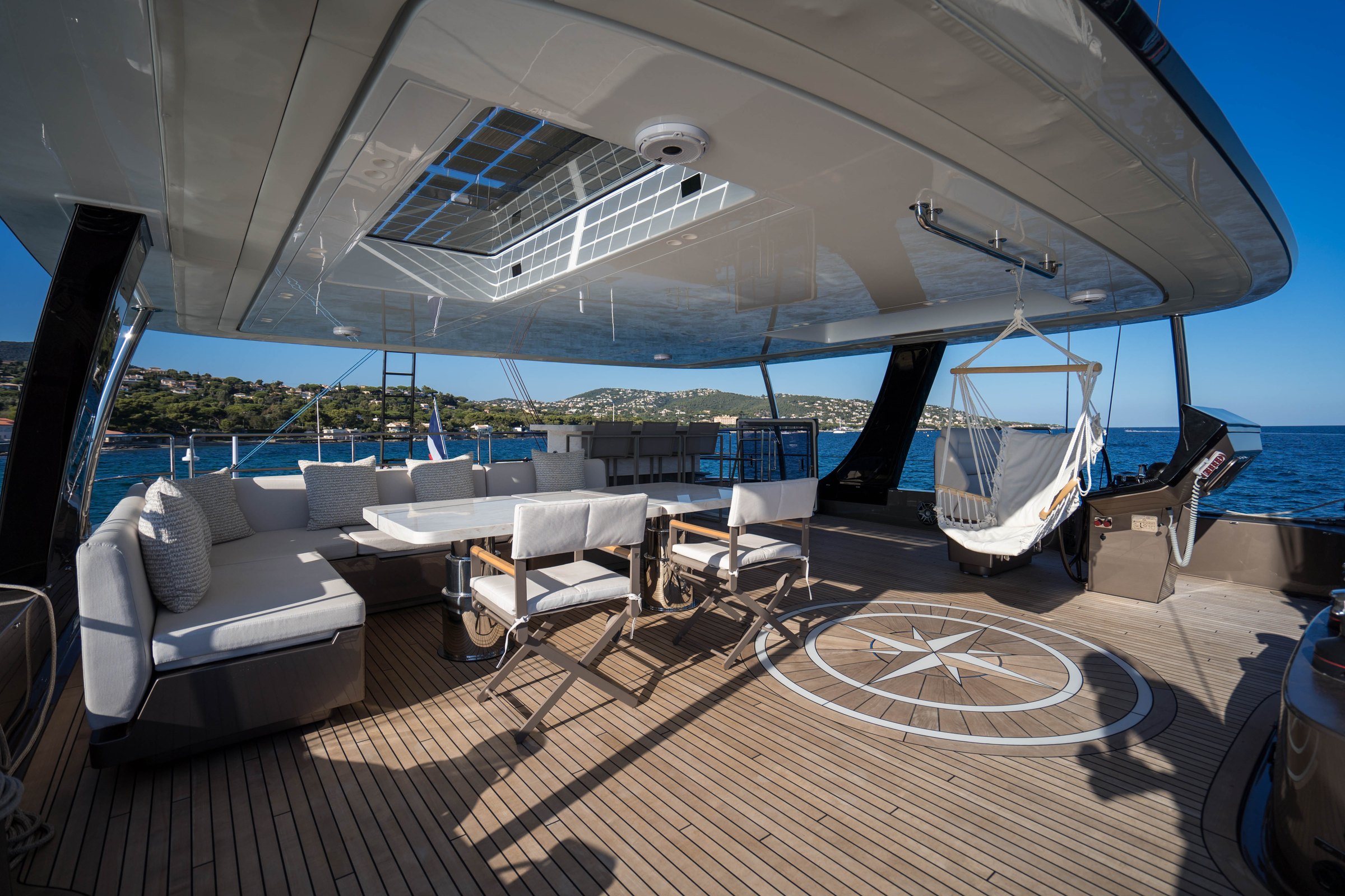 The flybridge of Āura, table, hammock chair and compass rose beneath the hardtop