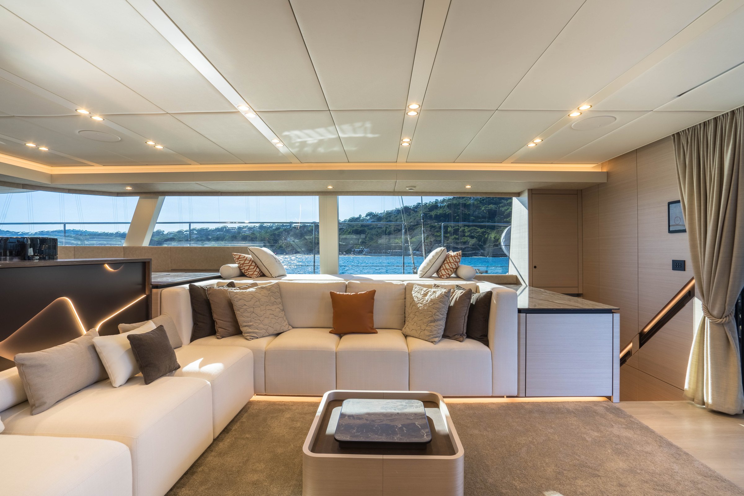 The lounge on Āura, U-shaped sofa and marble-topped coffee table in front of the windows