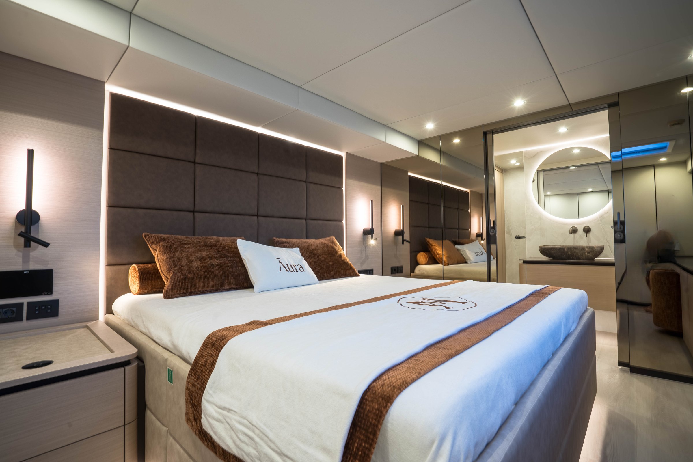 The master cabin of Āura, padded headboard and embroidered linen
