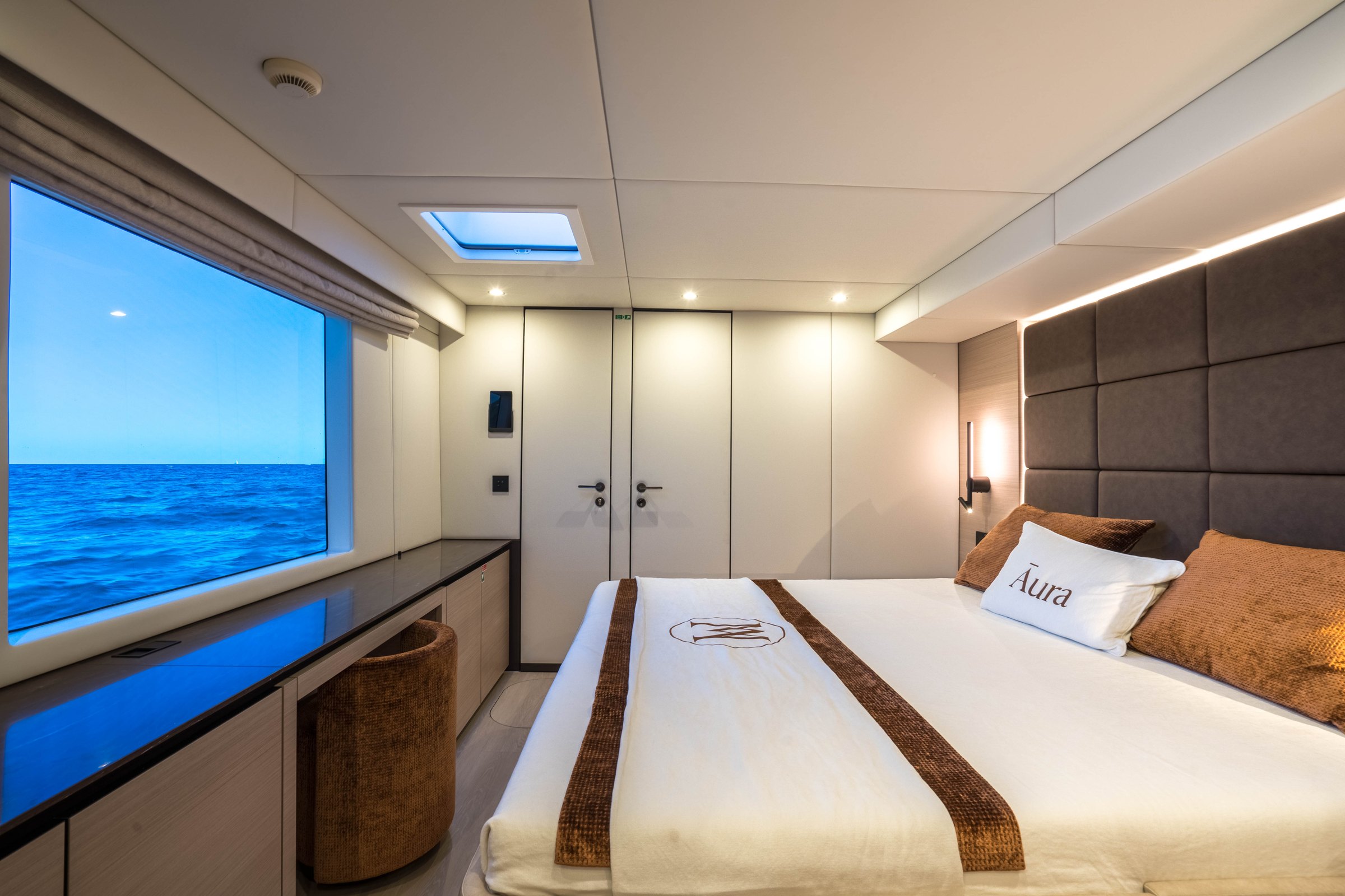 The master cabin on Āura, large hull window over the sea and embroidered linen