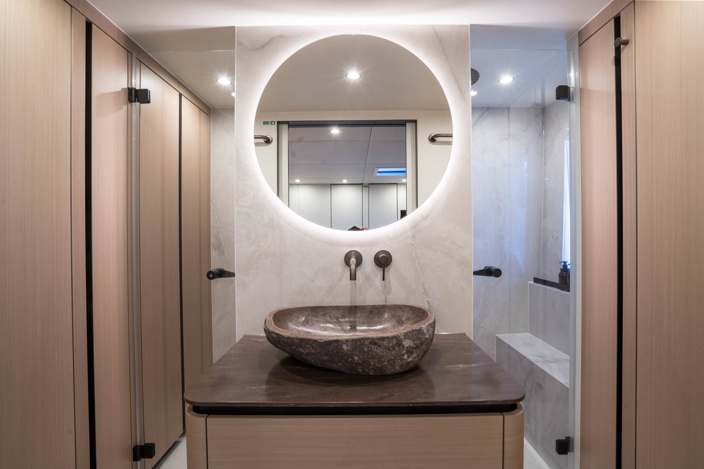 The master bathroom on Āura, stone basin and round mirror