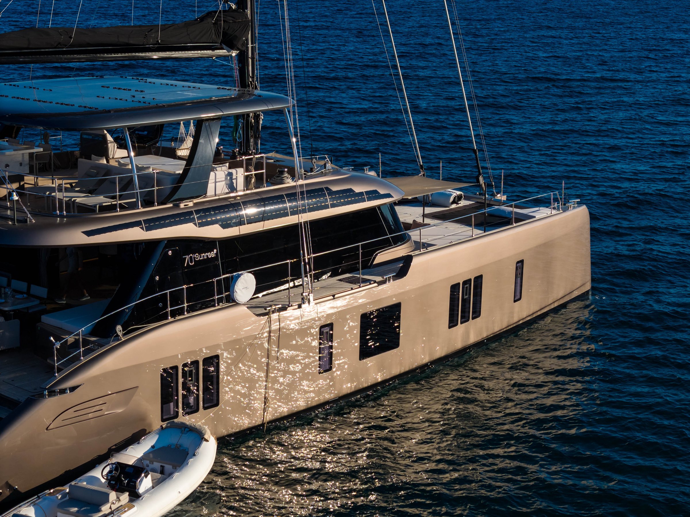 The hull side of Āura, a Sunreef 70 catamaran, in low sunlight, with her tender
